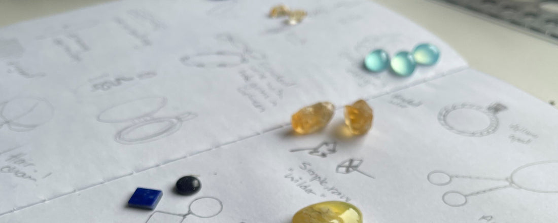 Close up of my sketchbook open on a bench with designs and gemstones laid out